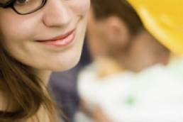 women smiling at camera with man in a hard hat in the background featured