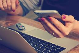 Woman holding her phone in front of her laptop