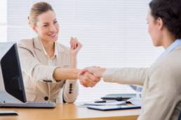 Smartly dressed young women shaking hands in a business meeting at office desk featured