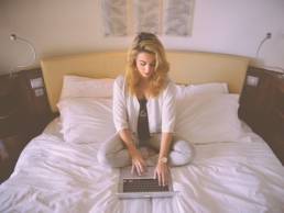 Blonde woman sitting on her bed whilst working on her laptop