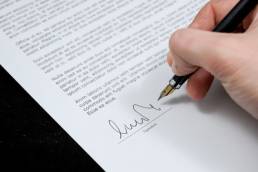 A shot of an individuals hand signing their name with a fountain pen