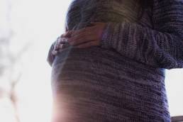 A shot of a pergnant woman in a grey jumper resting her hands on her bump
