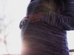 A shot of a pergnant woman in a grey jumper resting her hands on her bump