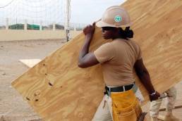 female apprentice construction worker carrying plank of wood featured