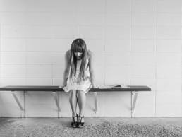 A woman sitting on a bench leaning over with her head down in grayscale.
