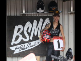 Vikki holding a red helmet, smiling outside a sign for the bike shed