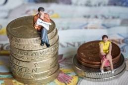 man-and-woman-sat-on-money-piles-gender-pay-gap-featured