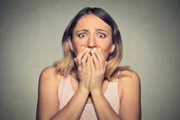 Blonde woman holding her hands up to her mouth looking scared
