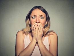 Blonde woman holding her hands up to her mouth looking scared