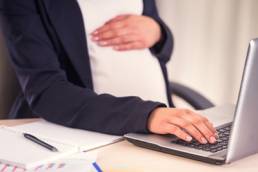 Pregnant woman holding baby bump whilst on the laptop at work
