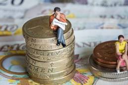 Man sitting on big pile of coins next to woman sitting on smaller pile of coins to demonstrate gender gap