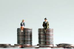 man and woman sitting on pile of coins, Equal Pay Day