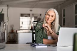 Portrait of happy senior woman holding eyeglasses and looking at camera at home. Successful old lady laughing and working at home, menopause