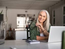Portrait of happy senior woman holding eyeglasses and looking at camera at home. Successful old lady laughing and working at home, menopause