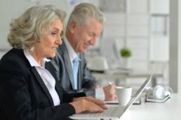 Older business man and woman on laptop, supporting older workers