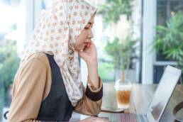 Young Thai Melayu female freelancer wearing hijab work using a laptop on wooden table in coffee shop. Modern woman life style.
