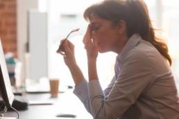 Exhausted female worker sit at office desk take off glasses feel unwell having dizziness or blurry vision, tired woman employee suffer from migraine or headache unable to work. Health problem concept