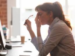 Exhausted female worker sit at office desk take off glasses feel unwell having dizziness or blurry vision, tired woman employee suffer from migraine or headache unable to work. Health problem concept