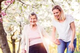 Elderly grandmother with crutch and granddaughter in spring nature, carer