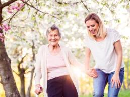 Elderly grandmother with crutch and granddaughter in spring nature, carer