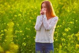 woman with hayfever standing in a field of flowers, allergies