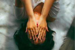 woman holding her head in her hands lying on bed, workplace performance anxiety 1