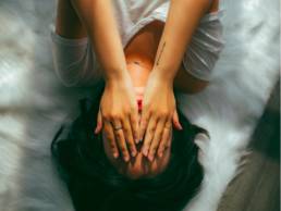 woman holding her head in her hands lying on bed, workplace performance anxiety 1