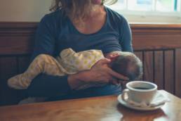 A young mother is breastfeeding her baby in a cafe while she is having a coffee