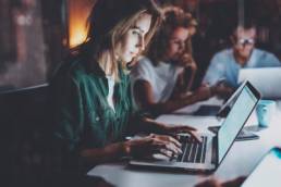 Team of young coworkers working together at night office.Young woman using mobile laptop at the table, workaholic