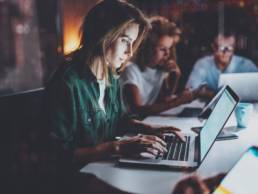 Team of young coworkers working together at night office.Young woman using mobile laptop at the table, workaholic