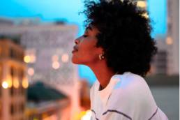 black woman looking out from balcony, wellbeing