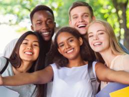 Cheerful international friends teenagers taking selfie while walking in summer park, young generation