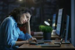 Tired, Overworked Female Financier Holds Her Head in Hands while Working on a Personal Computer