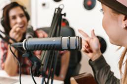 Close up of a happy woman singer performing at radio program while making podcast recording for online show, playing guitar