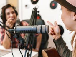 Close up of a happy woman singer performing at radio program while making podcast recording for online show, playing guitar