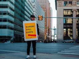 man holding a sign in the street, saying slavery still exists