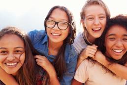 Four teenage girls having fun piggybacking outdoors, Reach Next Generation summit, empowerment