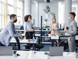 Modern team meeting, group work and social distancing. Manager with tablet speaks with workers in protective masks in interior of modern office with gadgets during coronavirus epidemic, free space
