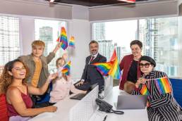 Business office workers from different ethnicities express support for self determination in LGBT. Business people showing LGBT flags in an office. Business people support Gender Equality