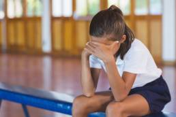 Sad schoolgirl sitting alone in basketball court at school gym, sexual harassment in school