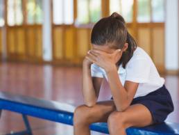 Sad schoolgirl sitting alone in basketball court at school gym, sexual harassment in school