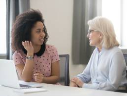 Diverse old and young female colleagues talking at work, african and caucasian business women sitting together in office having friendly conversation, mentor intern discussing planning shared project, Menopause