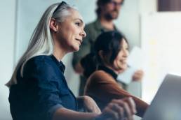 Senior woman with colleagues sitting by during business presentation, menopause, inclusion