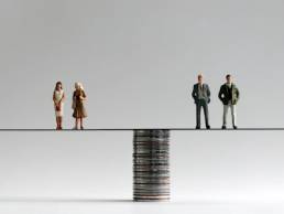 A group of miniature men and women standing on either side of a pile of coins, equal pay, gender pay gap