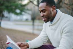 Man sitting down, reading book in park featured