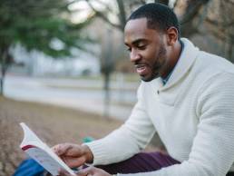 Man sitting down, reading book in park featured