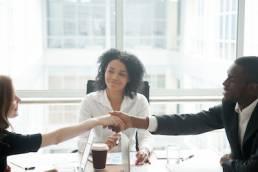 Smiling african businessman handshaking greeting caucasian businesswoman at group meeting negotiation, black satisfied entrepreneur welcoming partner shaking hand in lawyers office, respect concept, mediator