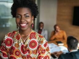 close up of beautiful young smiling professional black african business woman, coworkers hold a meeting in background, black female founders list
