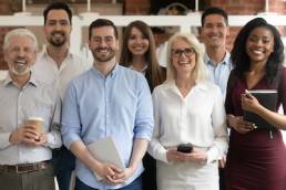 Happy diverse professional business team stand in office looking at camera, smiling young and old multiracial workers staff group pose together as human resource