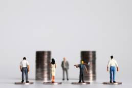 Miniature people with piles of coins, minimum wage, pay gap, pay transparency, equal pay